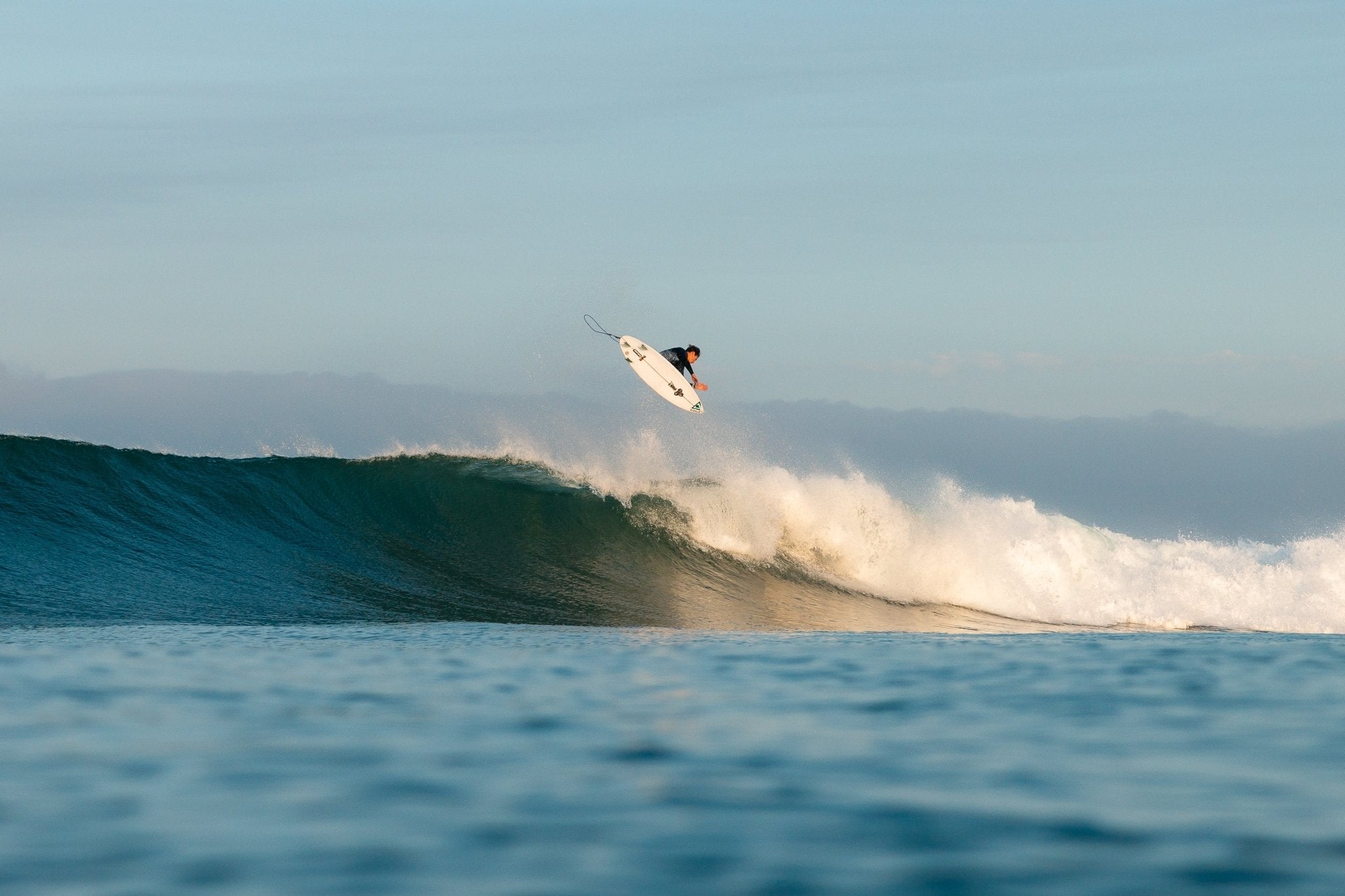 Surfer catching air above ocean wave in clear blue water at sunrise